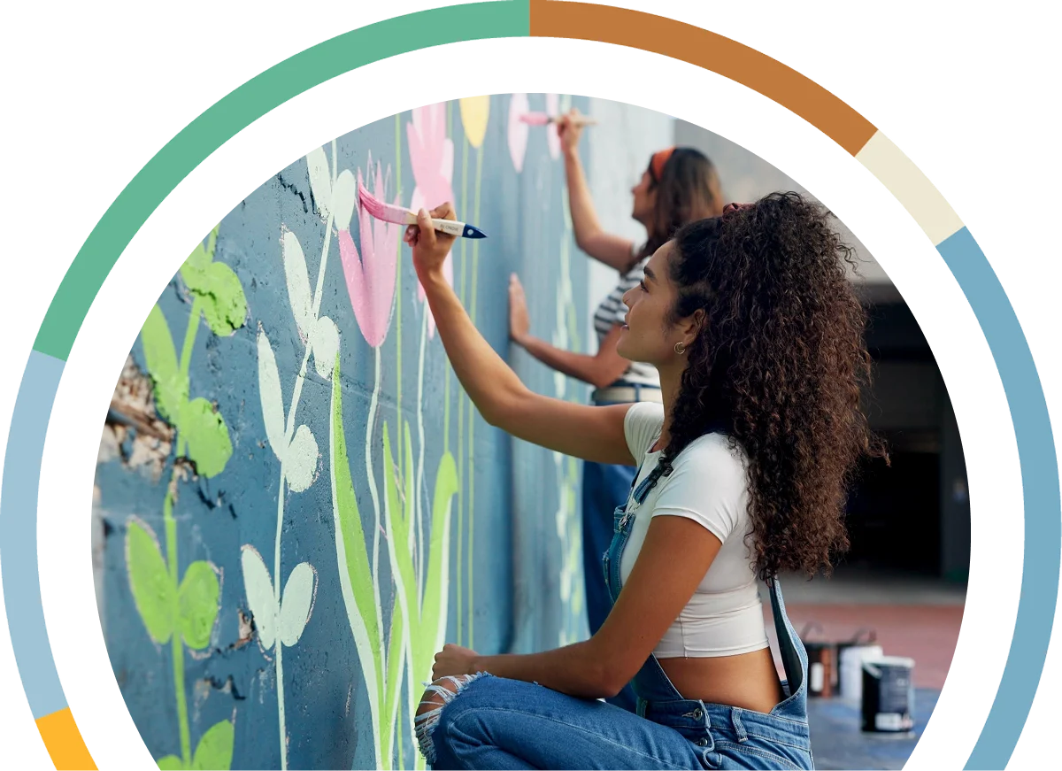 Young woman in overalls painting a mural with pink flowers