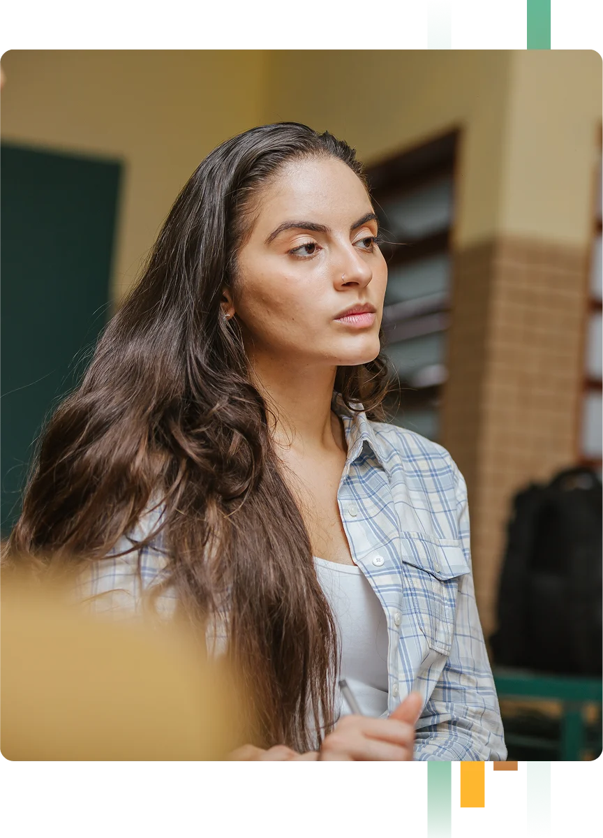 Intense, young woman focusing intently at something off screen while taking notes during class or meeting setting