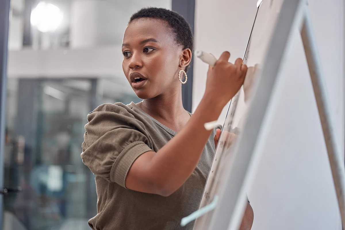 WOman standing at whiteboard drawing while talking to subjects off camera