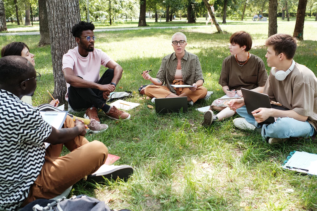 Group of students sitting in circle outside listening to professor teach