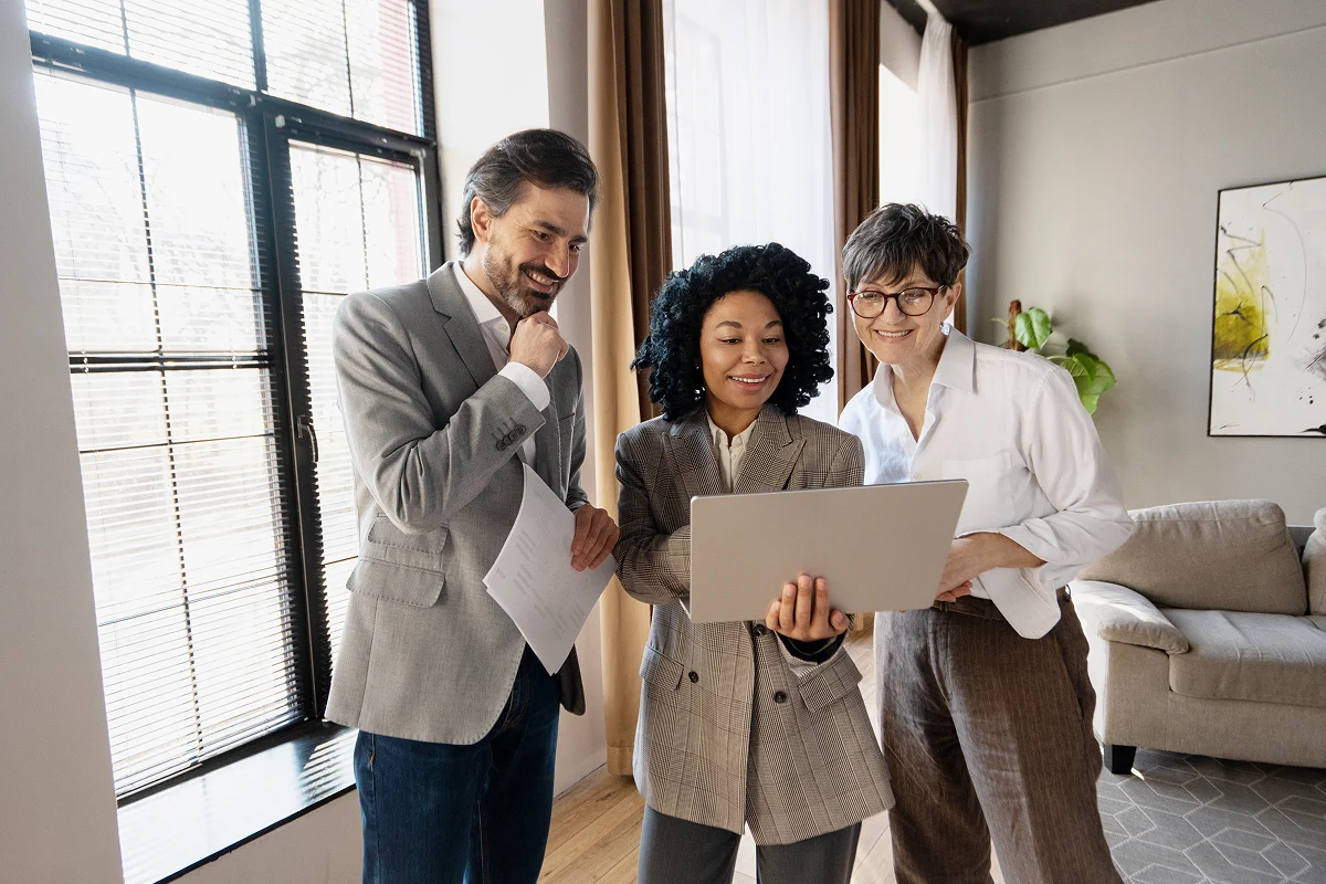 Three professionals gathered together and reviewing something on a laptop that is being held by the center subject